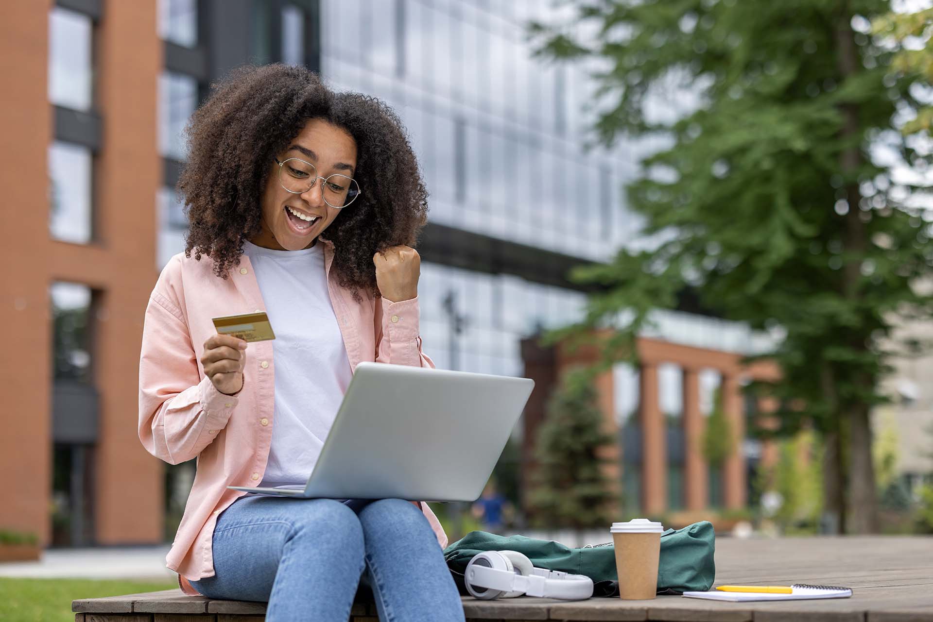 Excited african american woman shopping online with credit card and laptop in outdoor setting
